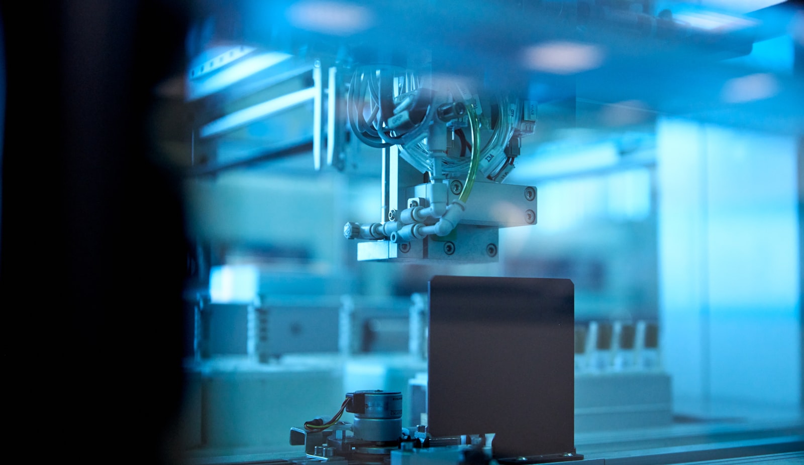 Automated robotic work cell running under blue light on a factory floor